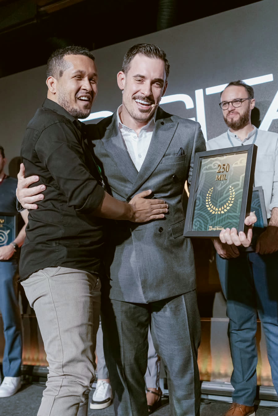 Aluno abraçado ao Renato, segurando a placa