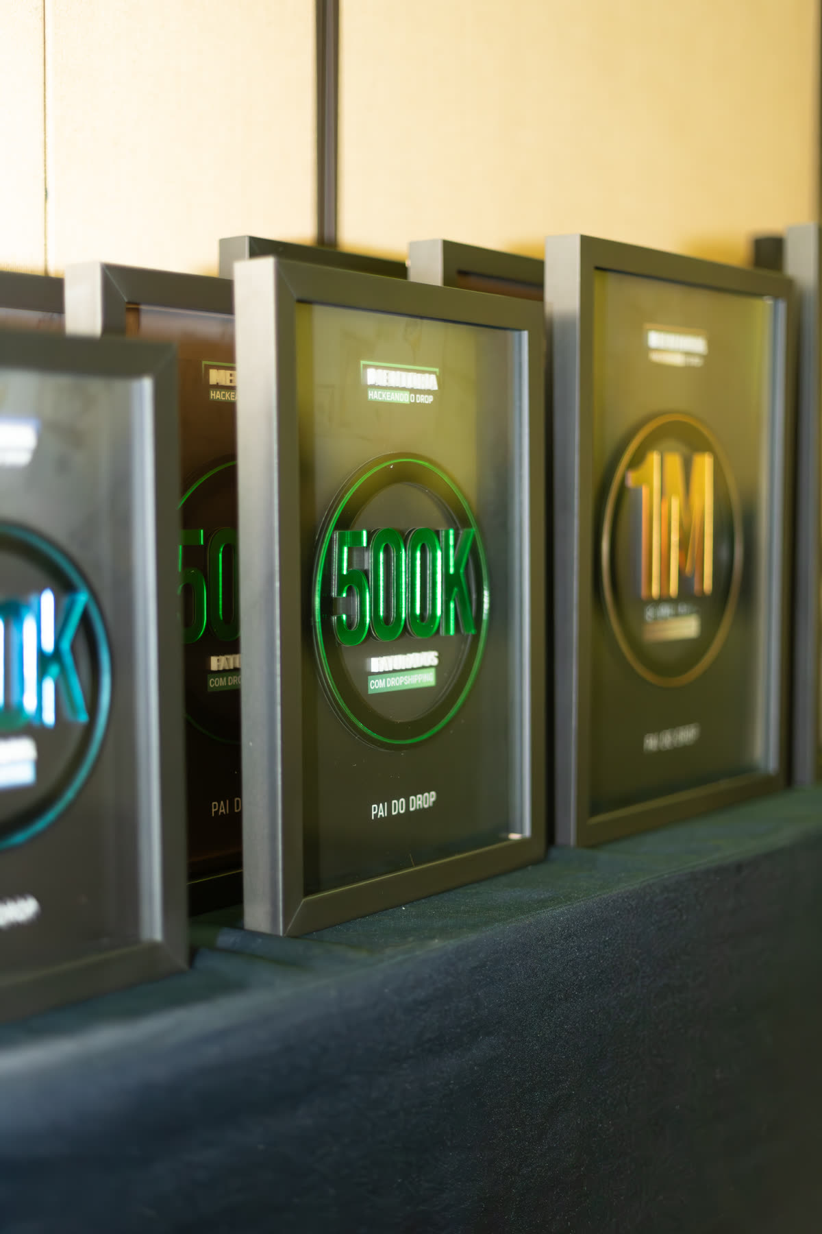 Placas de faturamento de 100 mil, 500 mil e 1 milhão enfileiradas numa mesa