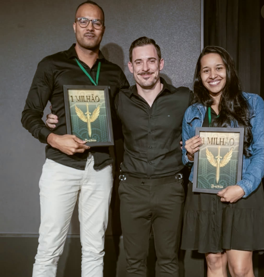 Renato no palco entre dois alunos, cada um segurando a placa de 1 milhão